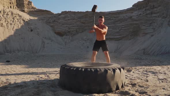 Muscle Athlete Strongman Man Hits a Hammer on a Huge Wheel in the Sandy Mountains in Slow Motion at