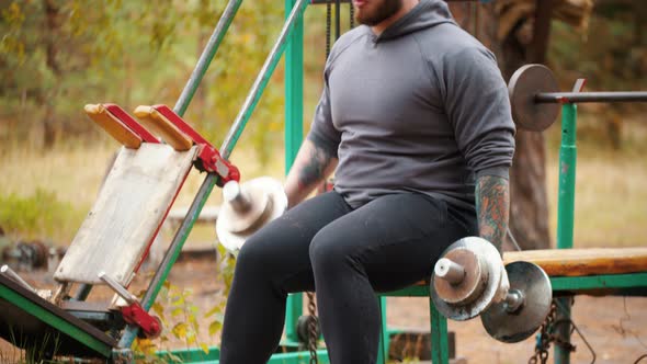 A Man Bodybuilder Pulling the Dumbbells in Both Hands - the Dumbbells Chained To the Bench -