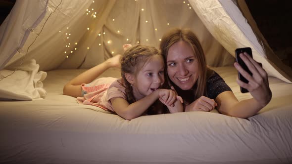 Happy Mother and Daughter Are Photographed on the Phone in a Makeshift Tent