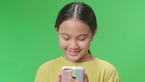 Smiling Young Asian Kid Girl Using Mobile Phone In Green Screen Studio alt