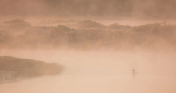 Calm Lake River And Man Fishing From Old Wooden Rowing Fishing Boat At Beautiful Misty Sunrise In