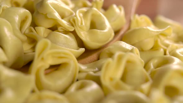 Raw dry Italian pasta tortellini in a full wooden spoon. Falling in slow motion
