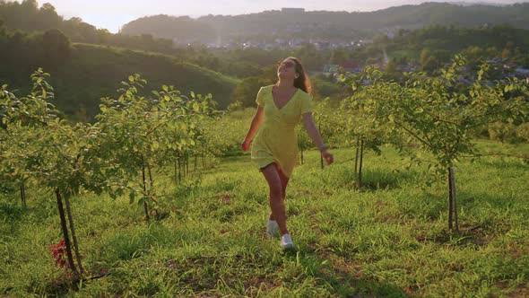 Happy Young Woman is Spending Summer Vacation in Country Running in Garden in Sunset Time