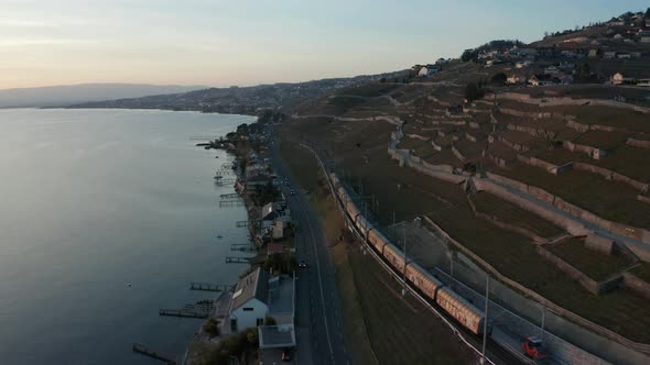 Aerial of freight train driving past highway near beautiful lake