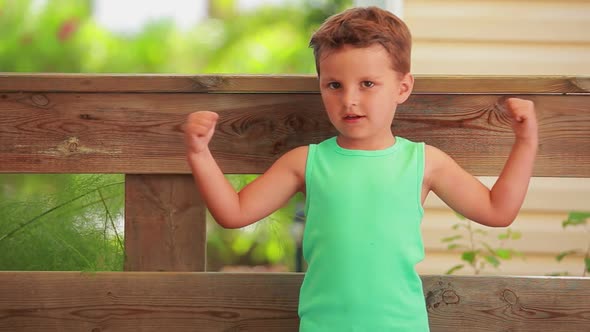 The Little Cheerful Boy in a Green T-shirt Is Showing Muscles