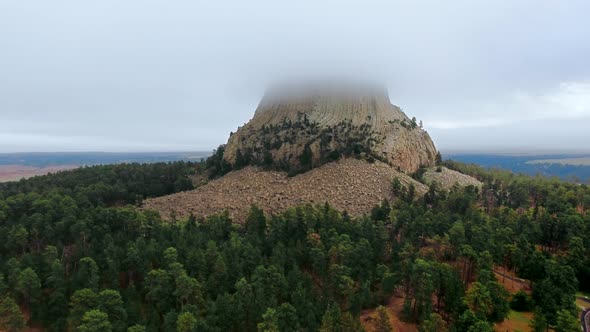 Drone footage of Devil's Tower rock surrounded by a dense forest in Wyoming, USA