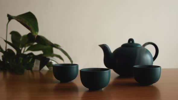 minimal background of a green japanese tea set with steam coming out of the cups, on a wooden table,