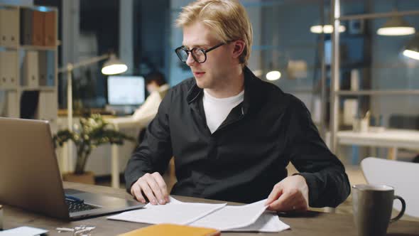 Businessman Signing Papers and Using Laptop during Night in Office