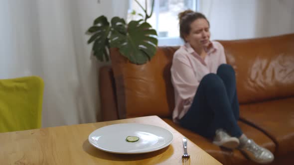 Focus on Plate with Cucumber Slice at Table and Crying Depressed Woman on Background