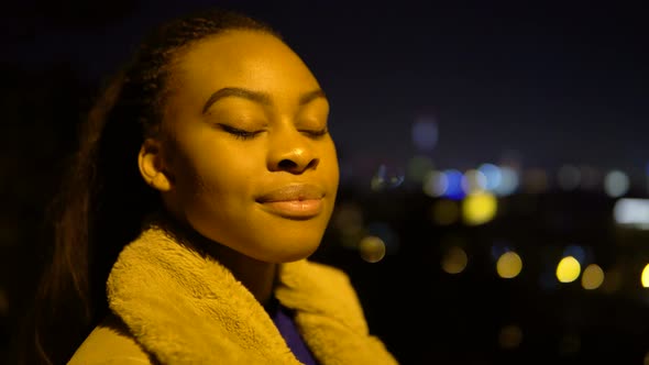 A Young Black Woman Looks Around and Smiles at the Camera in an Urban Area at Night  Side Closeup