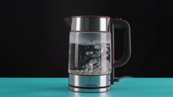 The Hand Takes a Glass Electric Kettle for Boiling Water for Drinks Tea or Coffee