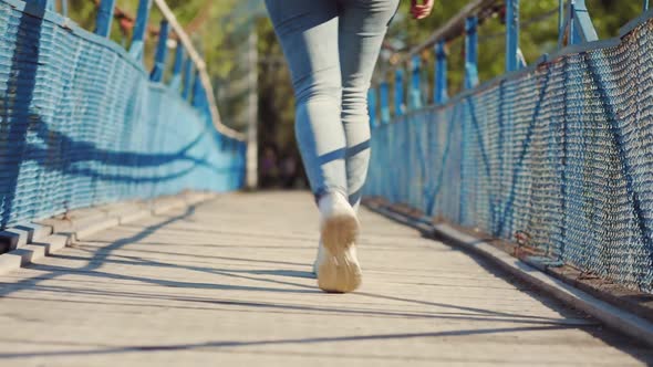 Female's Legs in Sneakers are Relaxed and Slowly Walking on the Bridge