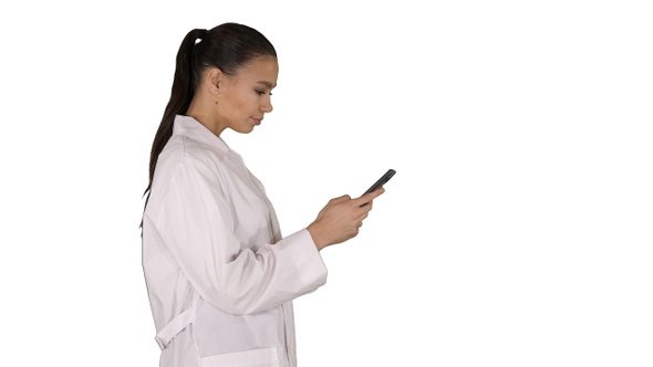 Cheerful cute young woman doctor typing text on phone while