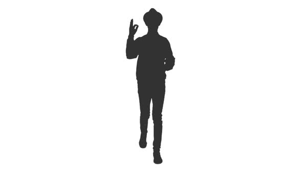Silhouette of Young Man with Hands in Pockets Showing OK Sign While Walking alt