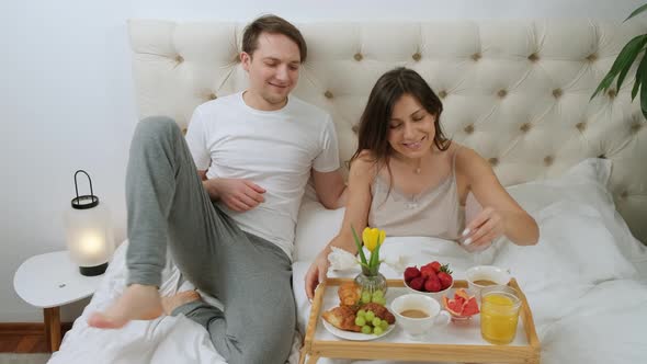 Woman Is Lying in Bed with the Breakfast While Her Husband Come and Kiss Her