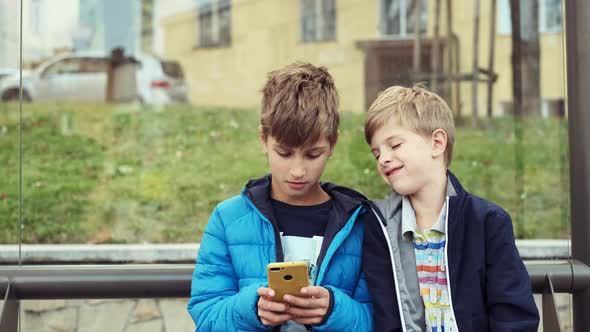 Two Boys Are Sitting At The Bus Stop.