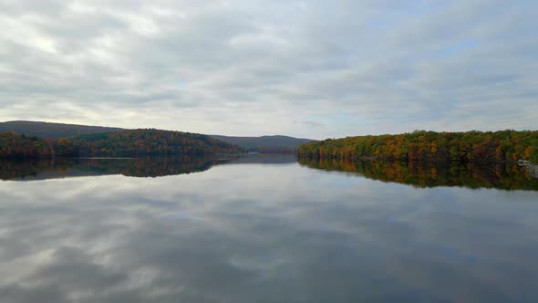 An aerial fly over a beautiful lake in the fall time showing the autumn foliage.