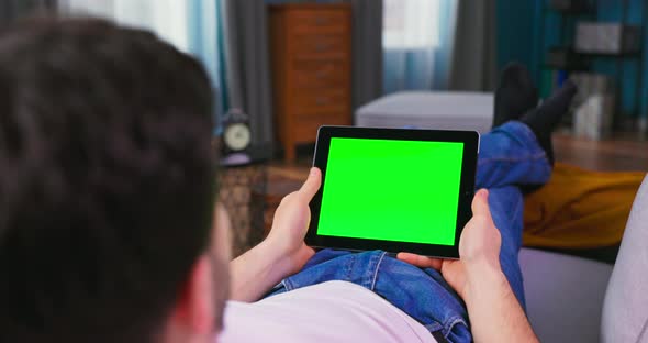 Young Man at Home Uses Green Mockup Screen Tablet