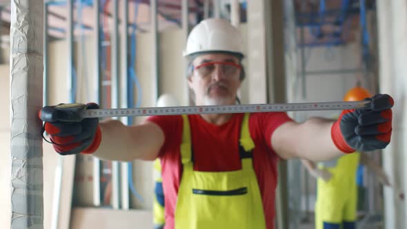 Middle-aged Builder Using Measuring Tape on Construction Site alt
