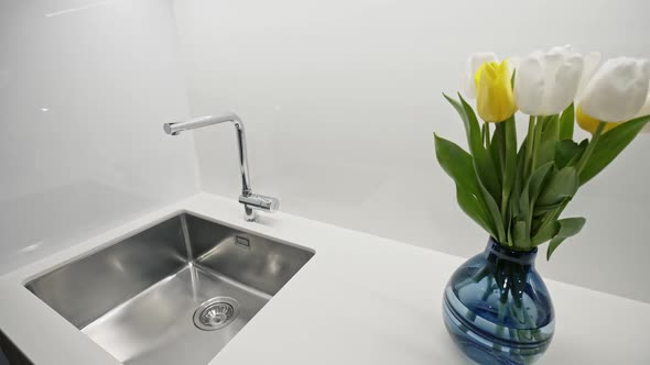 Camera Panning Left From Vase with Bunch of Fresh Tulips To Metal Sink with Faucet in Modern Kitchen