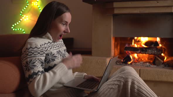 Young Woman Celebrates Success or a Happy Pose with a Laptop in Front of a Fireplace