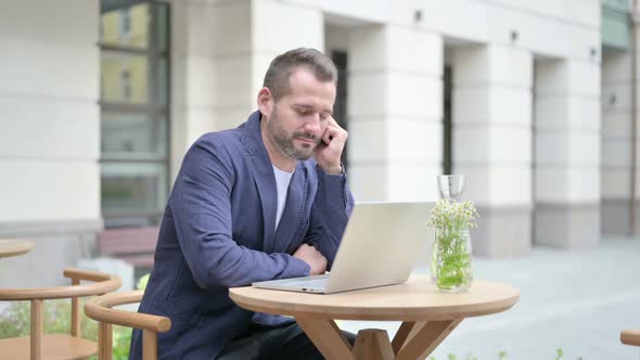 Man Falling Asleep While Using Laptop Sitting in Outdoor Cafe