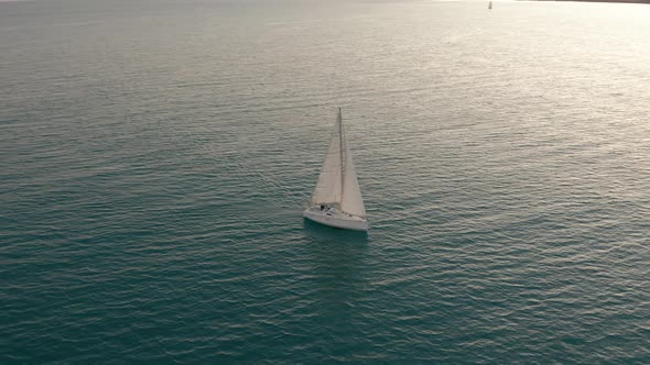 Aerial View. The Yacht Sails on the Sea at Sunset. Drone Flies Around the Yacht with Sails.