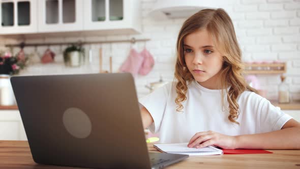 Portrait of Cute Little Girl Sitting at Kitchen Table Using Laptop for Distance Learning Slow Motion
