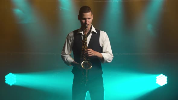 A Young Retro Stylish Guy Plays on the Golden Shiny Saxophone in the Turquoise Spotlights on Stage