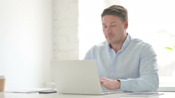 Man Showing Thumbs Up Sign While using Laptop in Office