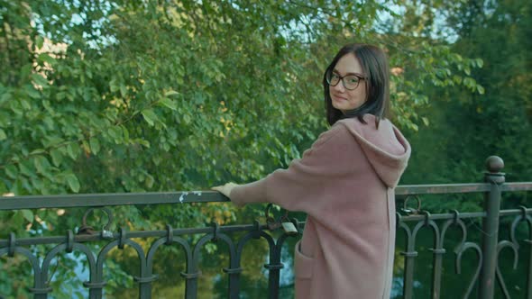 Young Happy Woman in Glasses Walks Along the Bridge in the City Park