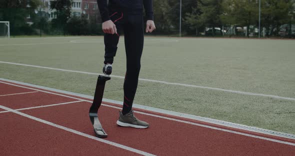 Crop View of Disabled Male Person with Prosthetic Running Blades Standing at Track on Sports Field