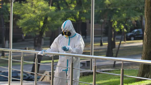 Unrecognizable, a Medic in a White Protective Suit Disinfects a City Street. A Virologist in a