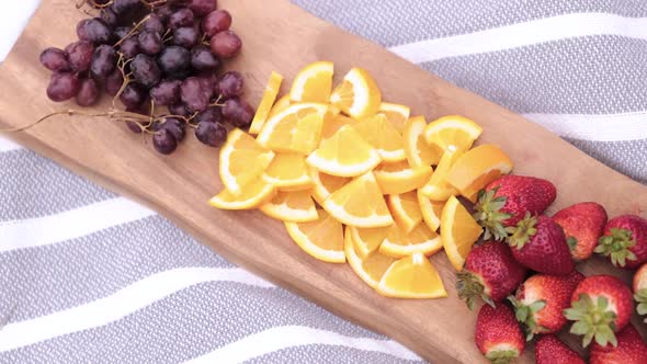 Top View of Sliced Fruit (Strawberries, Oranges, and Grapes) on Wooden Platter on a Blanket Outside