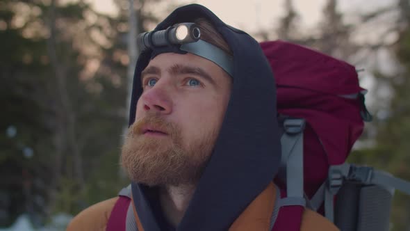 Bearded Tourist with Headlamp Looking around in Winter Forest