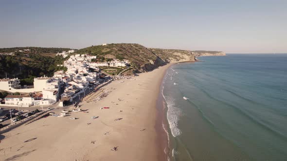 Waves washing on sand beach of Salema. White townhouses coastal village in Algarve, Portugal