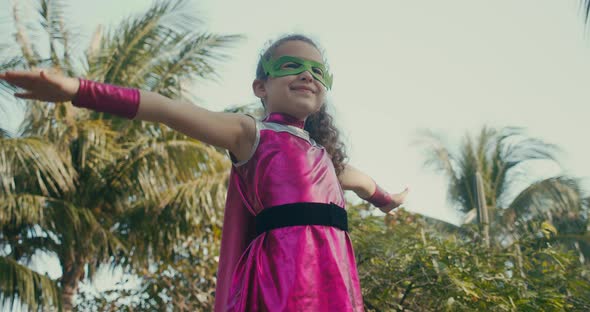 Kid Plays a Superhero Outdoors Cute Child in a Superhero Costume Dressed in a Pink Cloak and a Green