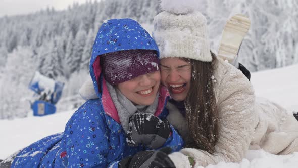 Two Young Women are Lying in the Snow and Laughing