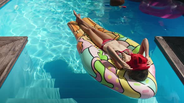 Confident Relaxed Caucasian Girl Sunbathing on Inflatable Swimming Mattress in Blue Pool Putting Red