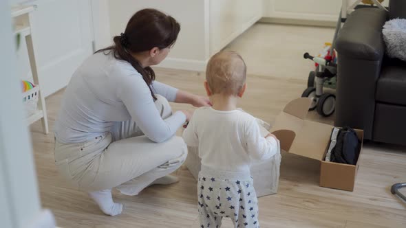 Mother with Baby Unpacking Unboxing Cardboard Package Box at Home Woman Received a Delivered Package