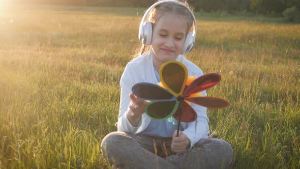 Teenage Girl Listening To the Music Sitting in a Green Meadow at Sunset.