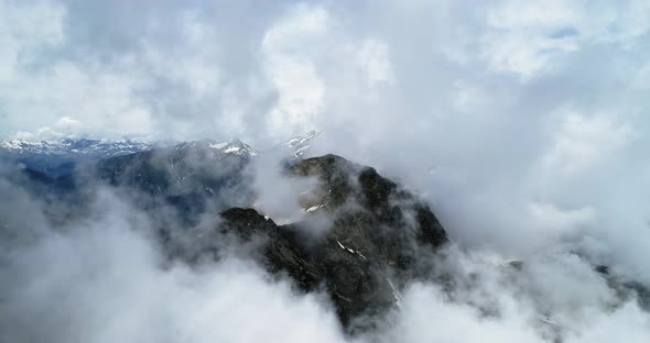 Forward Aerial Top View Over Cloudy Rocky Snowy Mountain in Sunny Day with Clouds