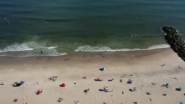 A bird's eye view over people relaxing on the beach on a sunny day. The drone camera truck right & t