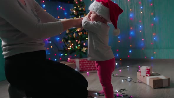 A mother teaches her child to walk. Festive decor and xmas tree on the background.