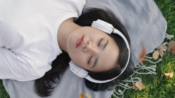 Beautiful young Asian female wears sunglasses and headphones sleeping on the grass.