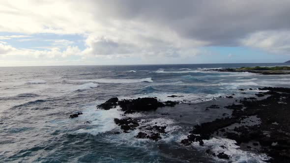 Drone flying above waves crashing on rocky shore in hawaii on a gloomy day