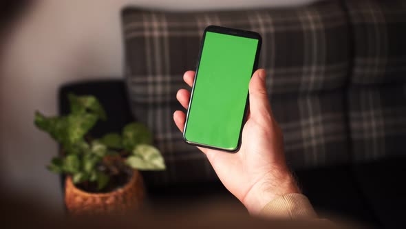 Handheld Camera: Point of View of Man at Modern Room Sitting on a Chair Using Phone With Green Mock