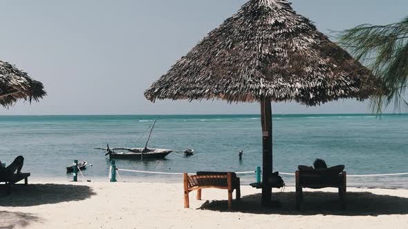 Thatched Umbrellas and Sun Loungers with Man on Sandy Beach By Ocean Zanzibar