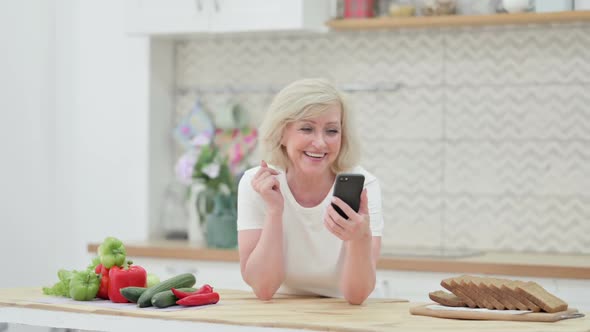 Old Woman Doing Video Call on Smartphone in Kitchen