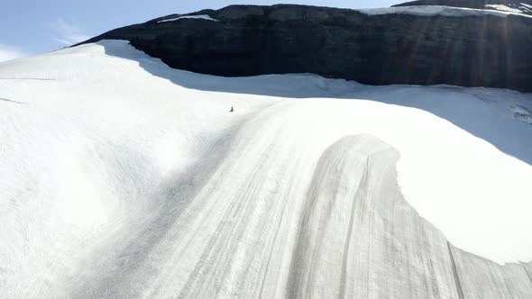 Aerial drone view following a snow mobile on a snowy glacier, in sunny Iceland